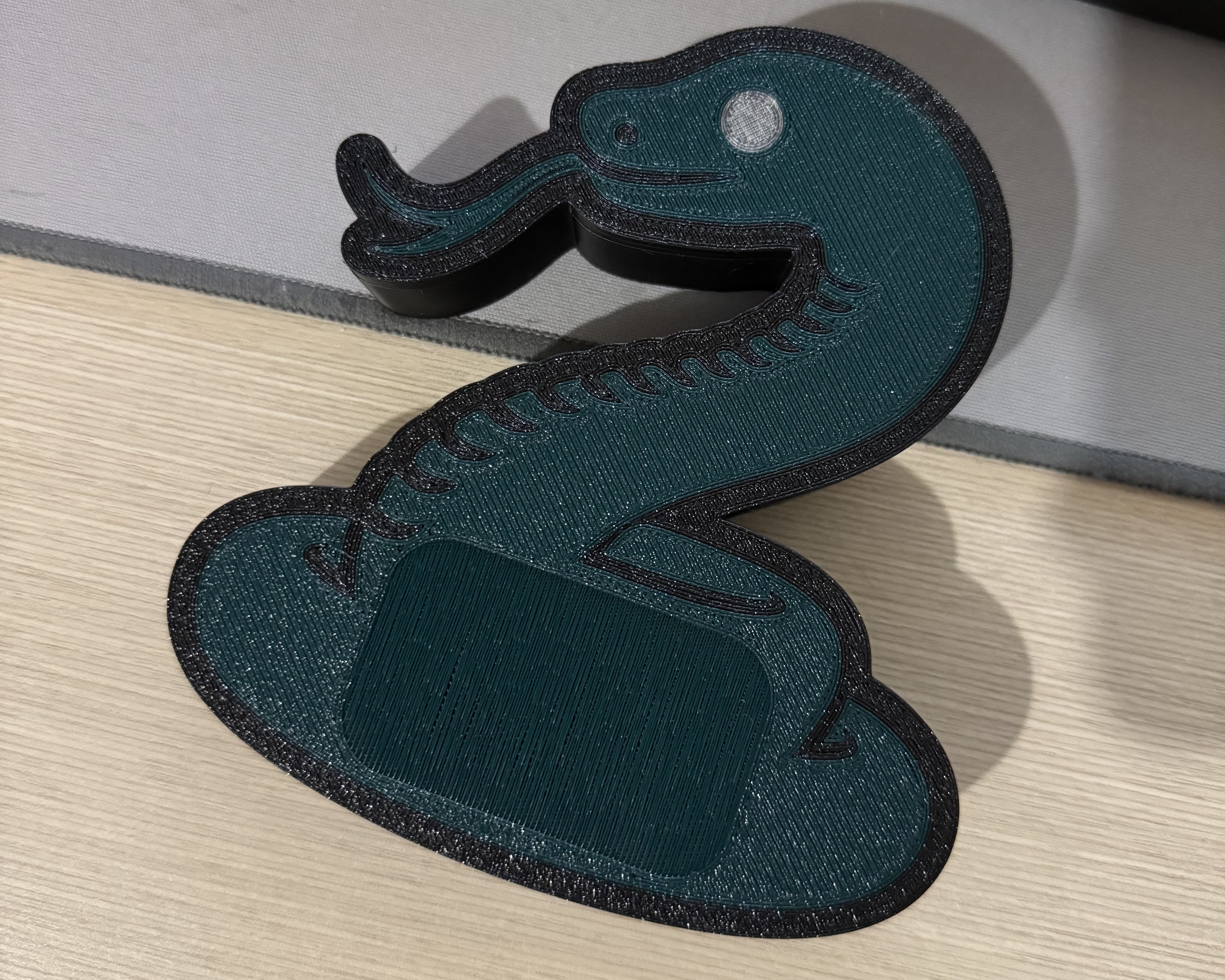 A dark-green container shaped like a stylised snake, with a textured surface.